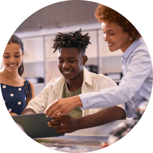 a teacher smiling while helping two students