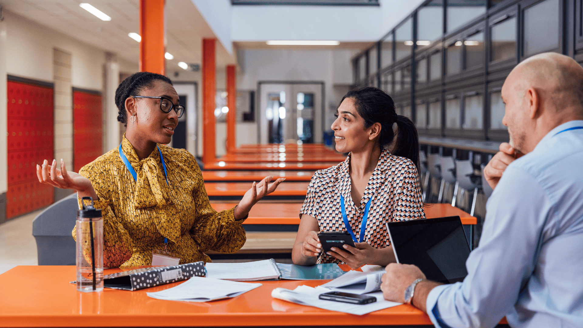 three teachers chatting at a table inside a school